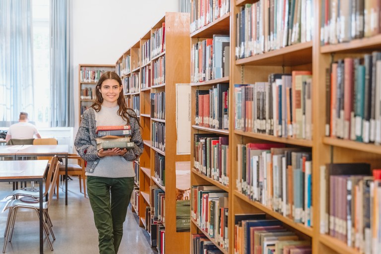 Eine Wissenschaftlerin und ein Wissenschaftler arbeiten hinter einer Glasfassade und mischen Chemikalien mit Großgeräten.