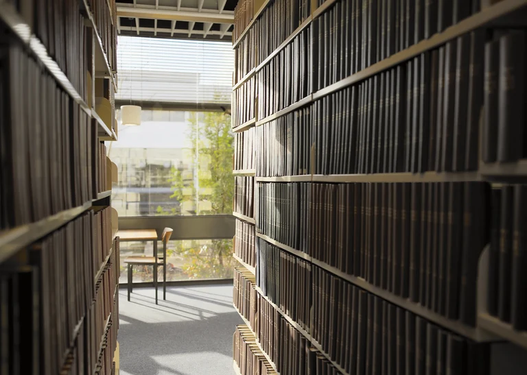 Eine Wissenschaftlerin und ein Wissenschaftler arbeiten hinter einer Glasfassade und mischen Chemikalien mit Großgeräten.