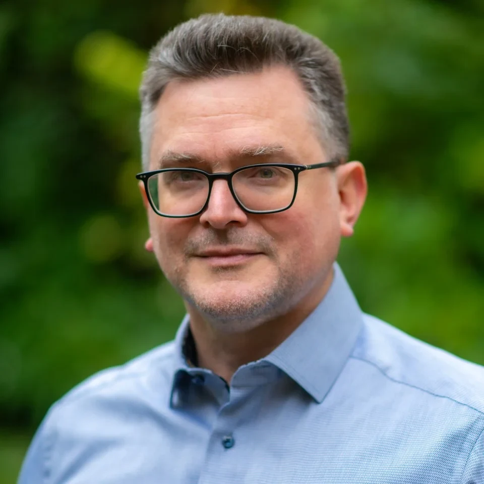 Eine Wissenschaftlerin und ein Wissenschaftler arbeiten hinter einer Glasfassade und mischen Chemikalien mit Großgeräten.