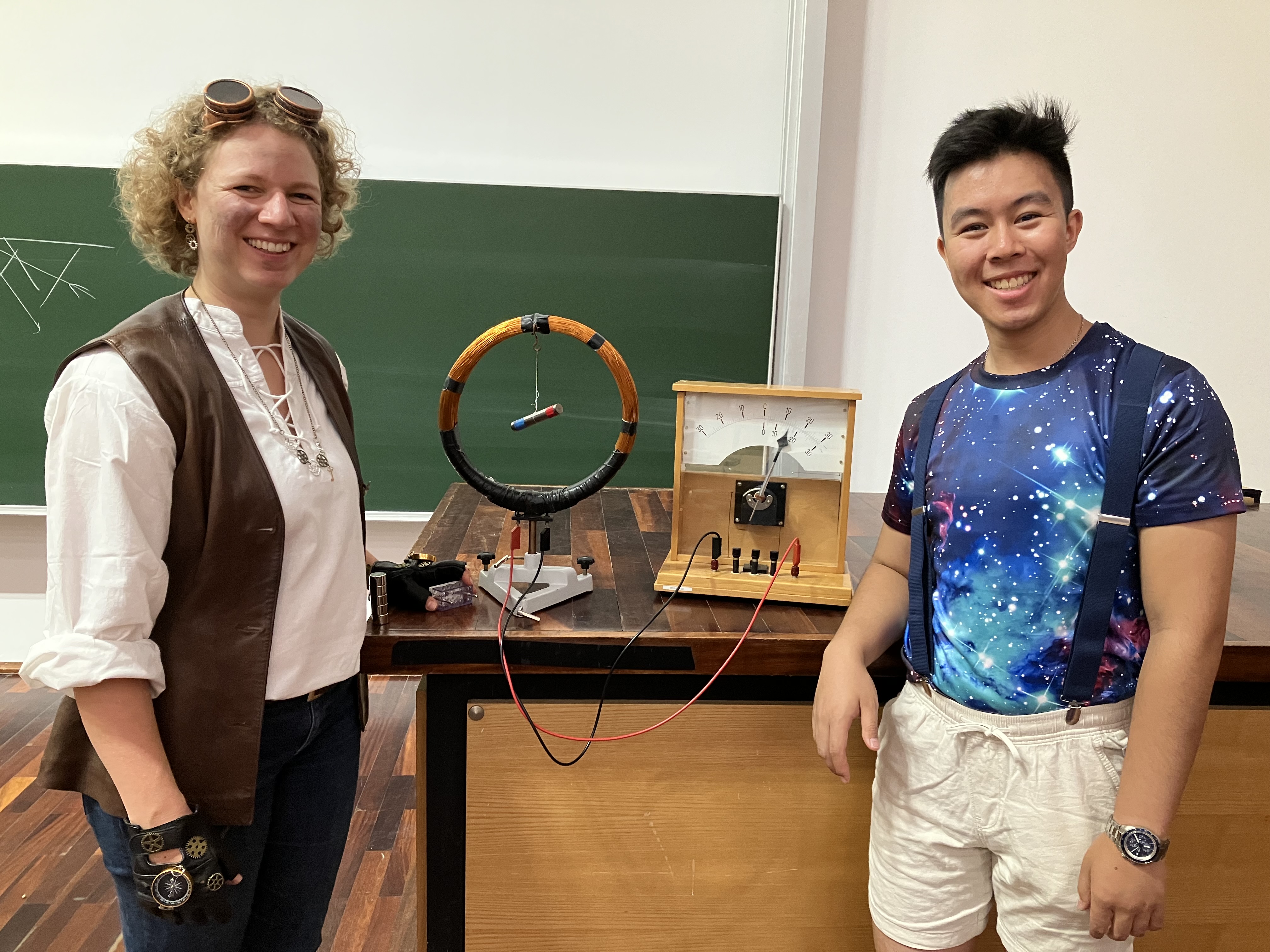On the left is a woman in a white shirt and brown vest, representing Humanity. On the right is a man with a mystical bluish printed T-shirt who embodies the Universe.